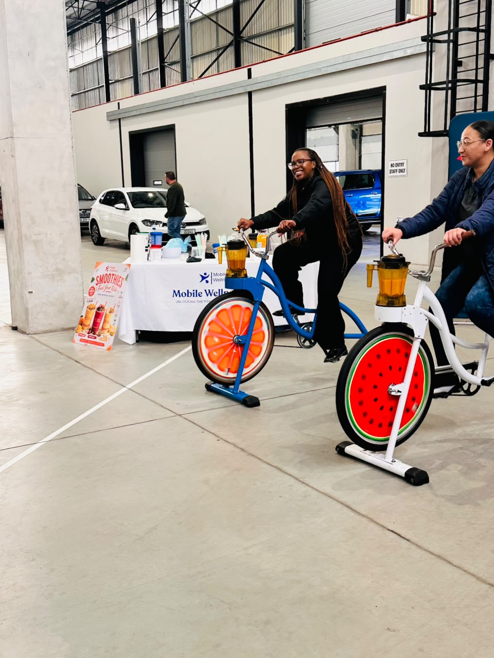 Two employees racing on Mobile Wellness Co. smoothie bikes at a corporate wellness day activation